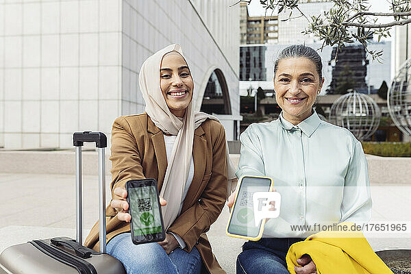 Smiling businesswomen showing vaccination QR certificate on mobile phones