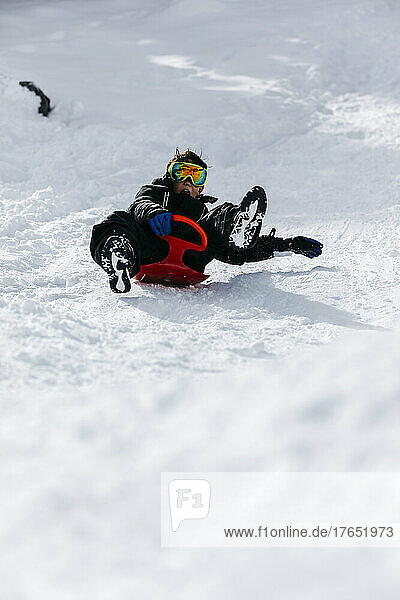 Playful boy wearing ski goggles tobogganing through snow