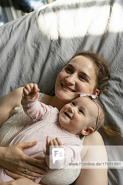 Happy mother with daughter lying on bed together at home