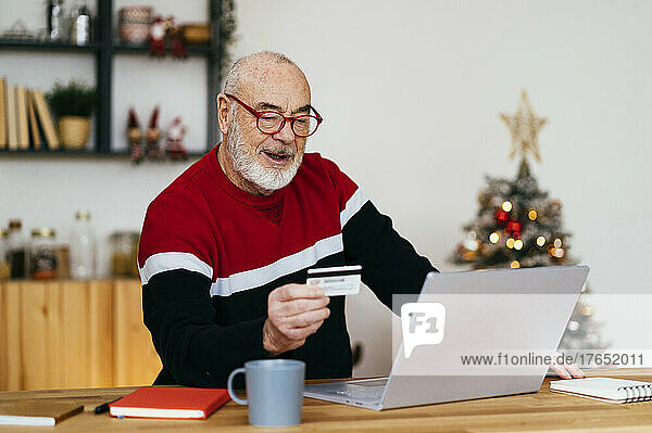 Senior man holding credit card doing online shopping through laptop at home