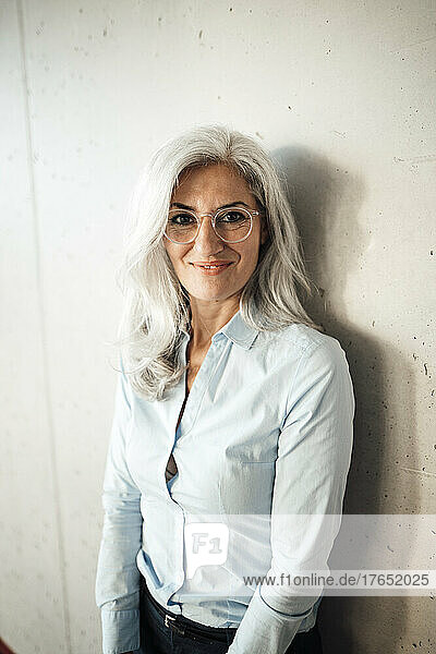 Smiling businesswoman wearing eyeglasses standing in front of wall