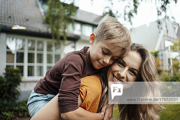Smiling blond woman giving piggyback ride to son at backyard