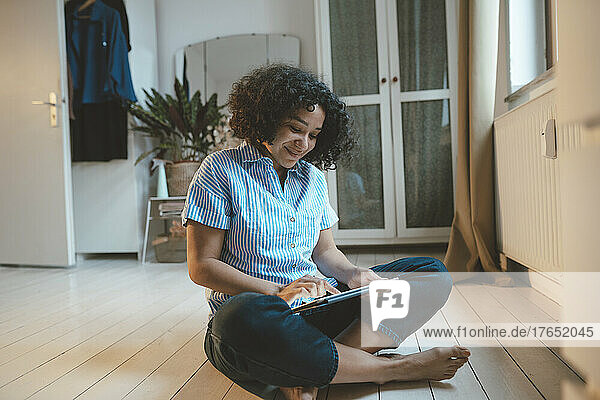 Smiling woman using tablet PC sitting on floorboard at home