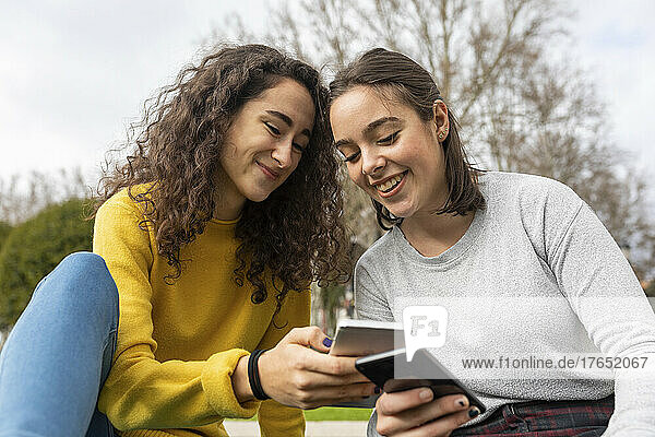 Happy friends using smart phones at park