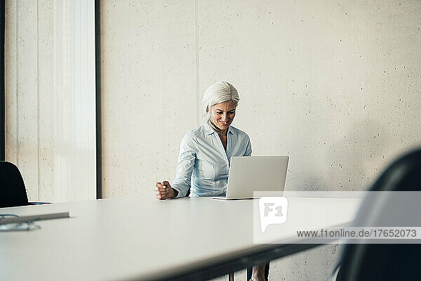 Smiling working woman using laptop sitting at desk in office