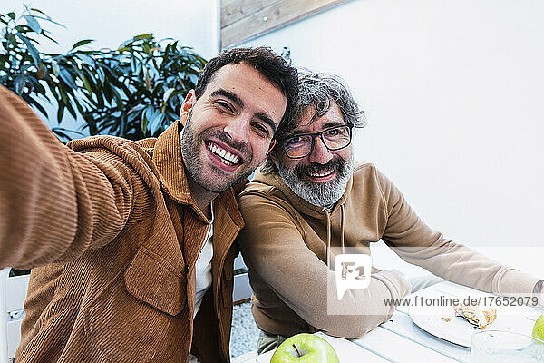 Glücklicher Vater und Sohn machen Selfie und frühstücken gemeinsam