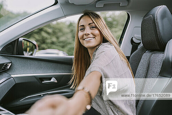 Glückliche blonde Frau hält Händchen und sitzt auf dem Beifahrersitz im Auto