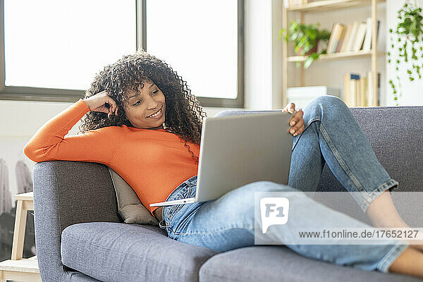 Smiling young woman using laptop sitting on sofa at home