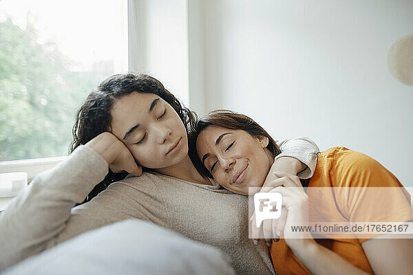 Teenage girl embracing mother and resting on sofa at home
