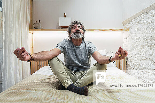 Senior man meditating on bed at home