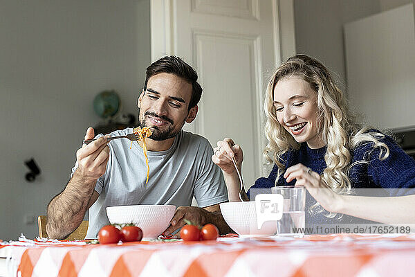 Man and woman eating food sitting on dining table at home