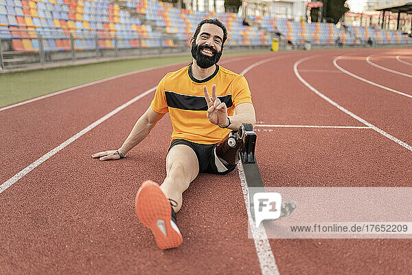 Lächelnder Mann mit Beinprothese sitzt auf der Laufstrecke und zeigt ein Friedenszeichen