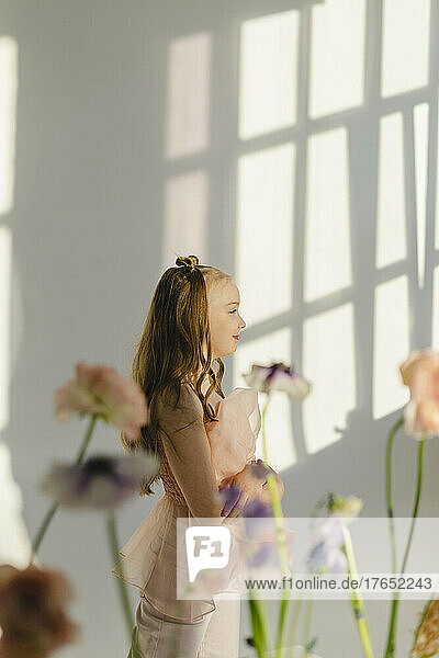 Smiling girl standing behind flowers by white wall