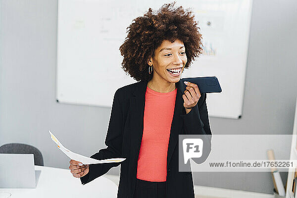Happy businesswoman with document talking on mobile phone in office