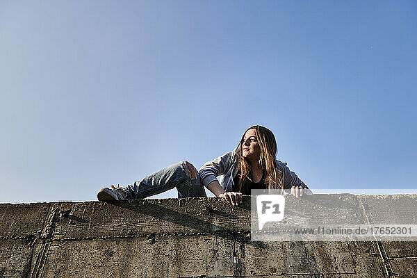 Young woman climbing over concrete wall