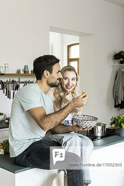 Couple eating noodles sitting on kitchen counter at home