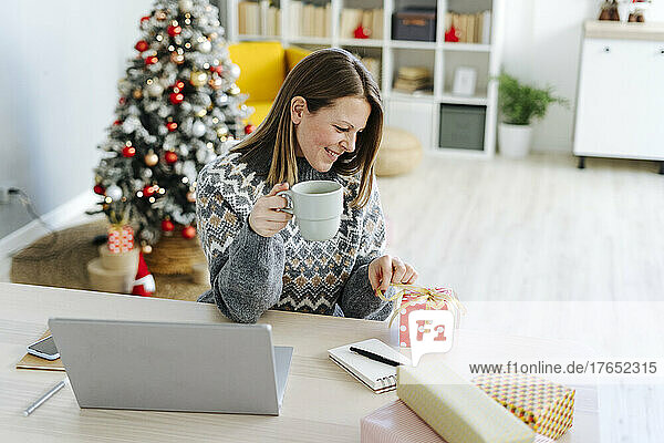 Smiling woman holding coffee cup looking at Christmas present