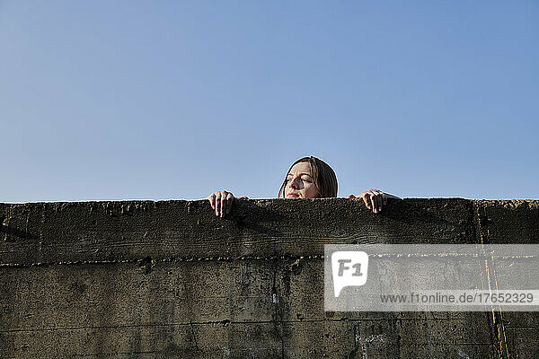 Young woman looking over concrete wall