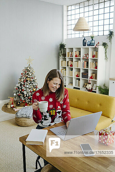 Happy woman holding coffee cup using laptop at table