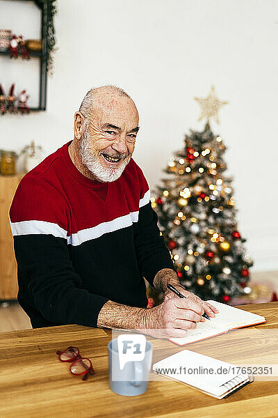 Glücklicher älterer Mann mit Tagebuch  der am Tisch sitzt