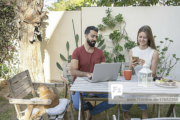 Smiling couple with laptop and smart phone sitting in back yard