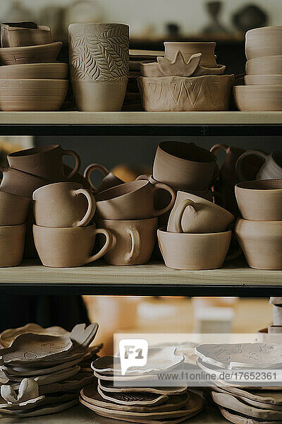 Tonschüsseln mit Tassen und Tellern auf einem Regal in der Werkstatt angeordnet