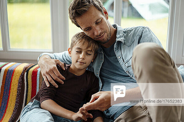 Father sitting by son with eyes closed on sofa at home