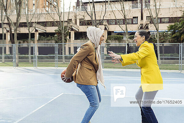 Cheerful businesswomen playing basketball at sports court