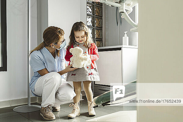 Dentist with cute little girl holding stuffed toy at dental clinic