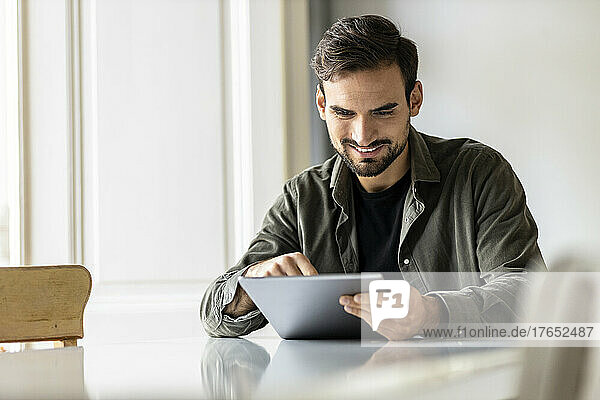 Smiling man sitting at table using tablet PC at home