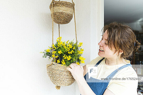 Lächelnde Frau pflanzt in einen Korb  der vor der Wand hängt