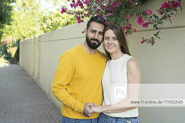 Smiling couple holding hands standing in front of wall