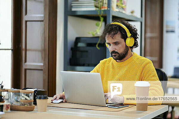 Businessman listening music through headphones using laptop at desk in office