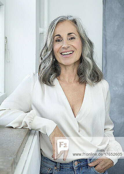 Lächelnde Frau mit grauen Haaren  die am Fenster steht