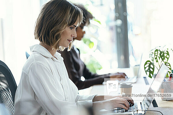 Businesswoman with colleague using laptop at desk in office