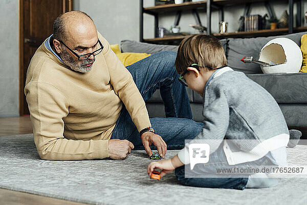 Senior man and grandson playing with toy car in living room at home