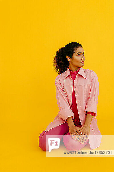 Young woman wearing pink shirt sitting against yellow background