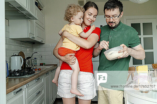 Man holding bowl standing by woman carrying daughter in kitchen