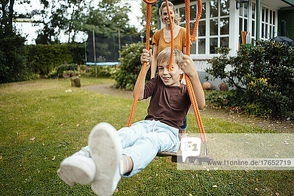 Smiling boy swinging in front of mother at backyard