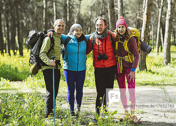 Smiling friends standing together in forest on sunny day
