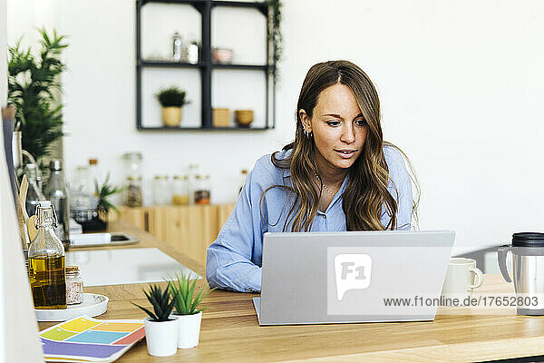 Freelancer using laptop sitting by kitchen counter at home