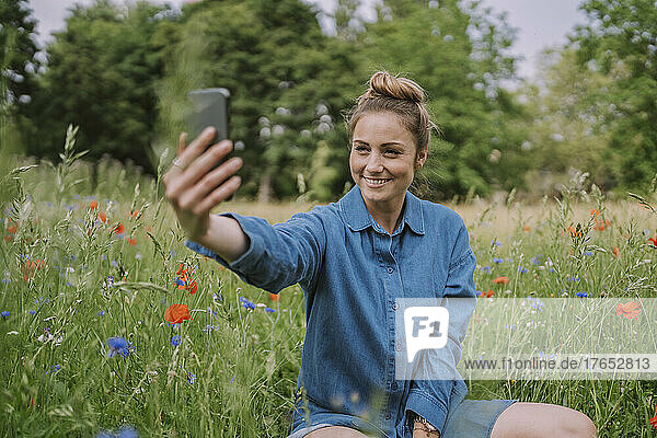 Smiling woman taking selfie through smart phone in meadow