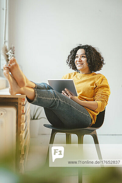 Happy beautiful woman sitting with tablet PC on chair at home