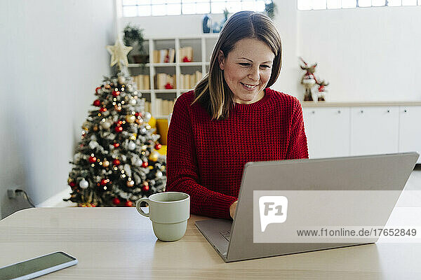 Smiling woman with laptop and coffee cup sitting at table