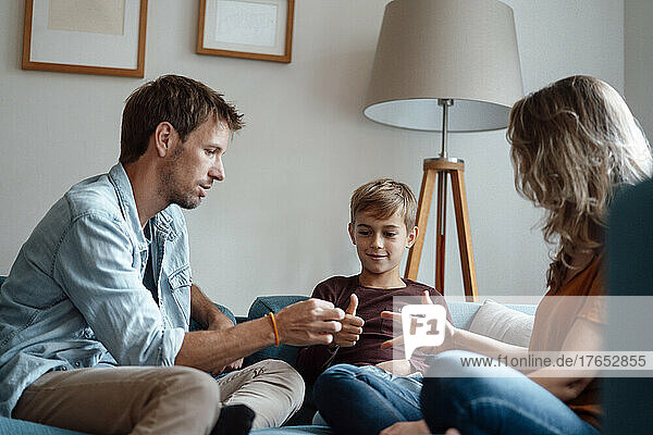 Parents playing rock paper scissor with son sitting on sofa at home