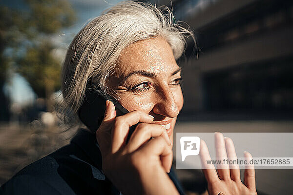 Lächelnde Geschäftsfrau  die an einem sonnigen Tag mit dem Handy telefoniert