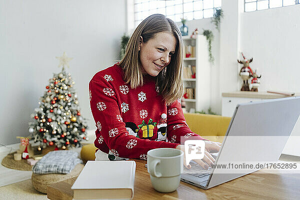 Smiling blond woman using laptop at table in living room