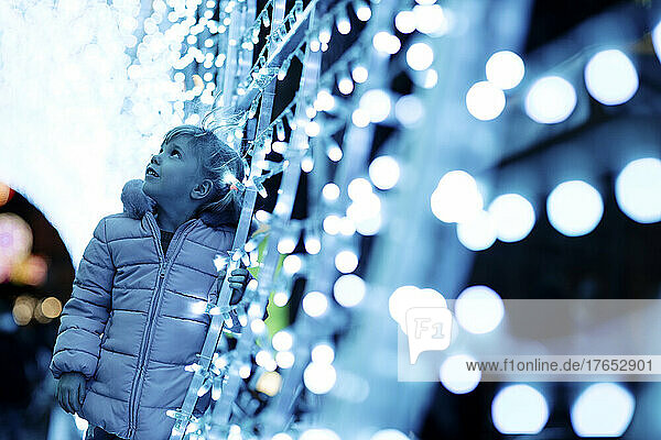 Cute girl standing by illuminated Christmas lights