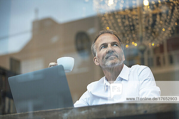 Businessman with coffee cup and laptop sitting in cafe