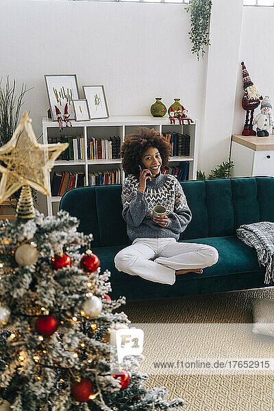 Happy woman talking on mobile phone sitting on sofa in living room